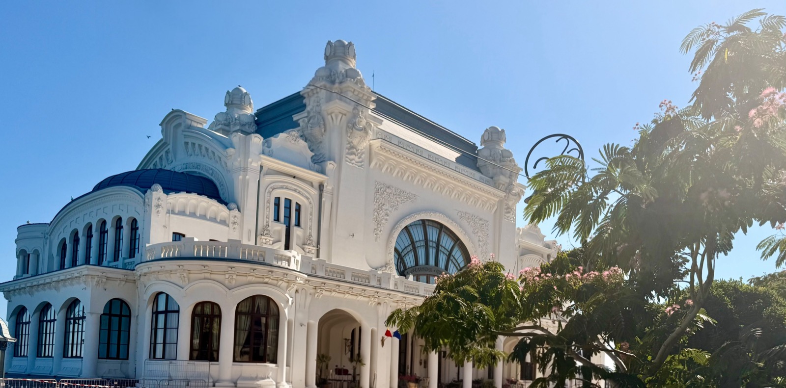 Cazinoul văzut din lateral, cu cupola albastră, ornamentele Art Nouveau și un arbore de mătase înflorit în dreapta