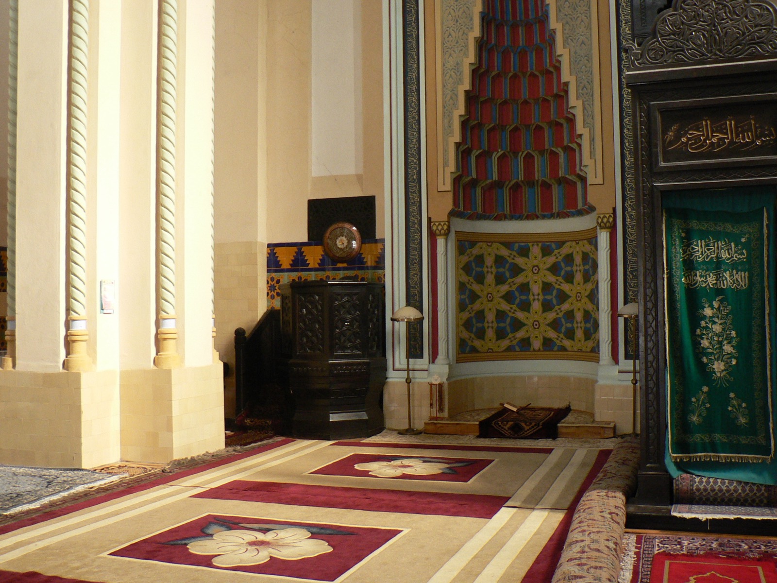 Im Inneren der Moschee: der orientalisch verzierte Mihrab, geschnitzte Holzeinrichtung und Teppiche auf dem Boden