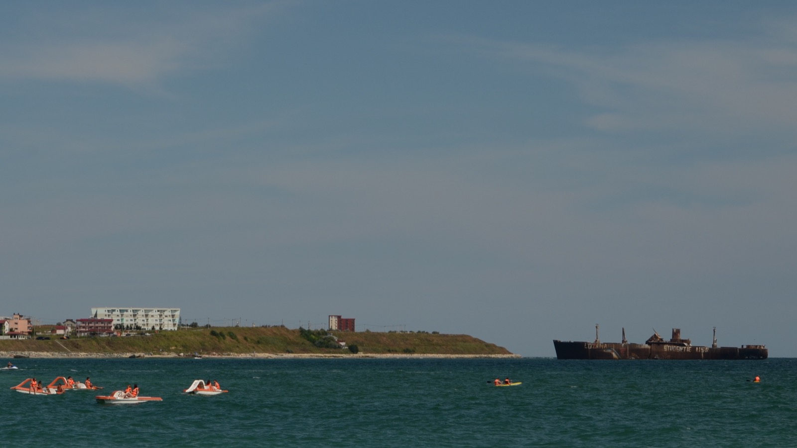 Pedalos on the sea at Costinești, with the headland north of the resort and the Evangelia wreck behind
