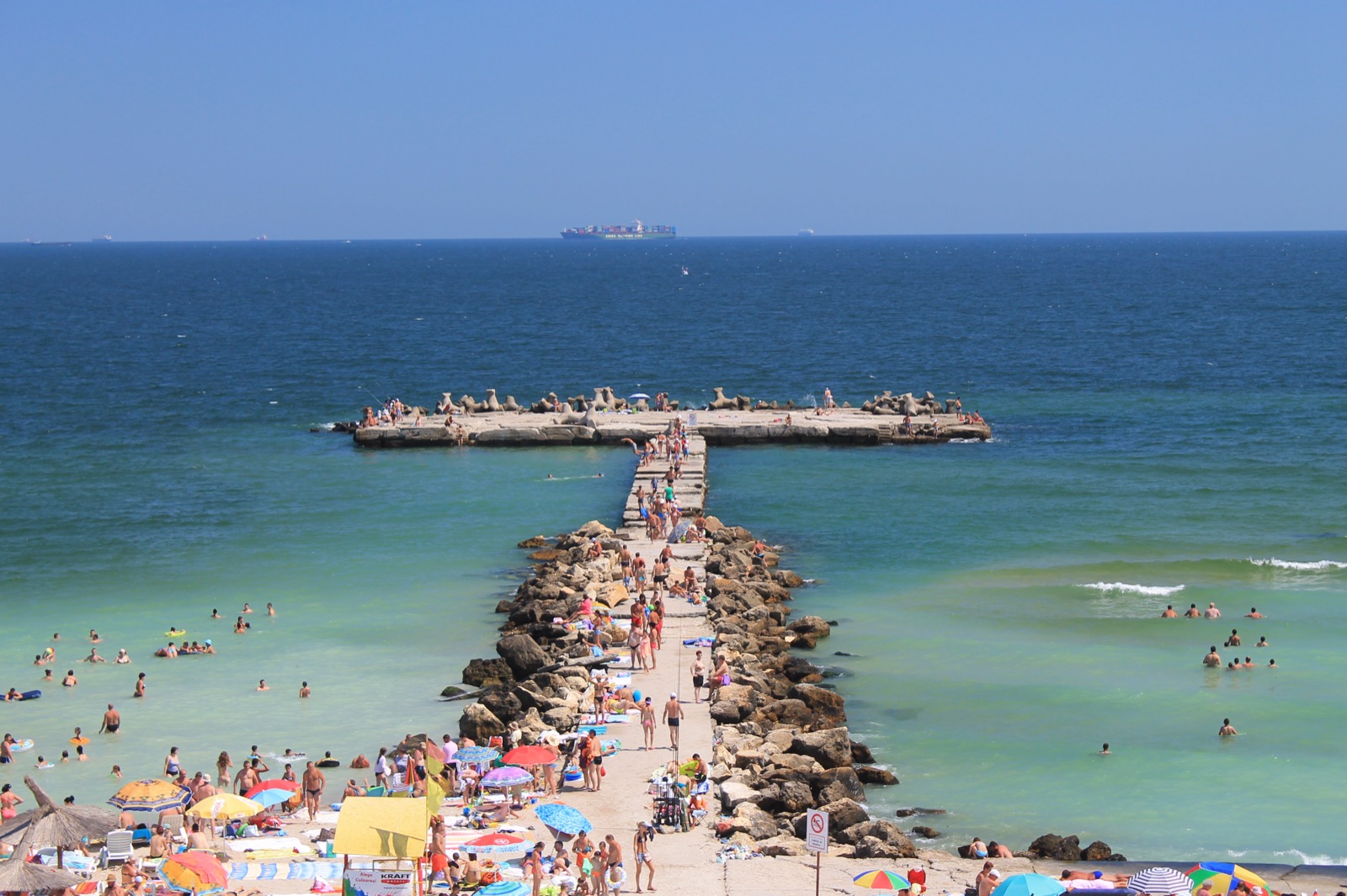 Dig de piatră în formă de T care intră în mare de pe plaja din Eforie Nord, cu apa turcoaz de o parte și de alta