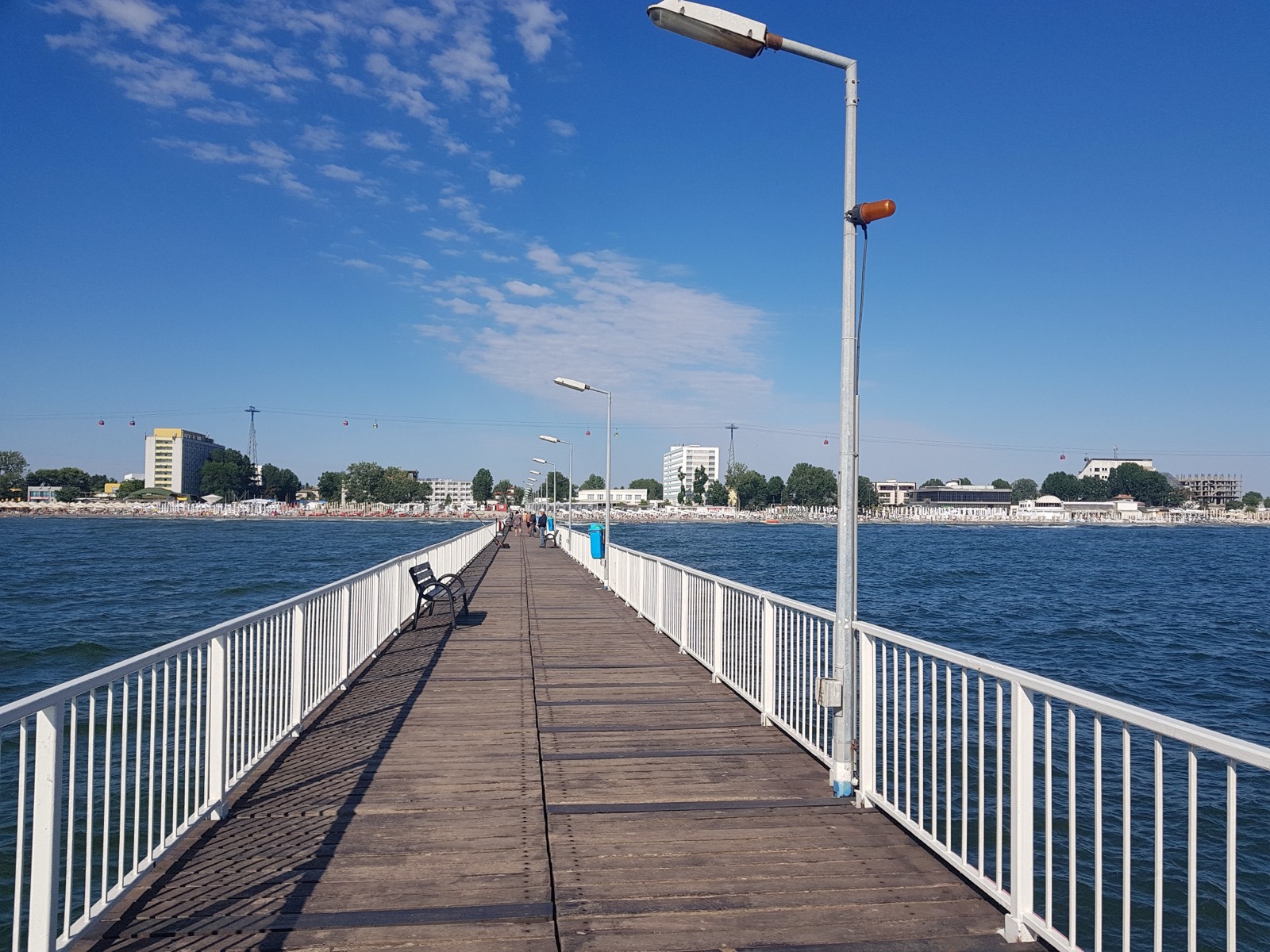 Debarcaderul de lemn care intră în mare, cu plaja, hotelurile și cabinele telegondolei în fundal