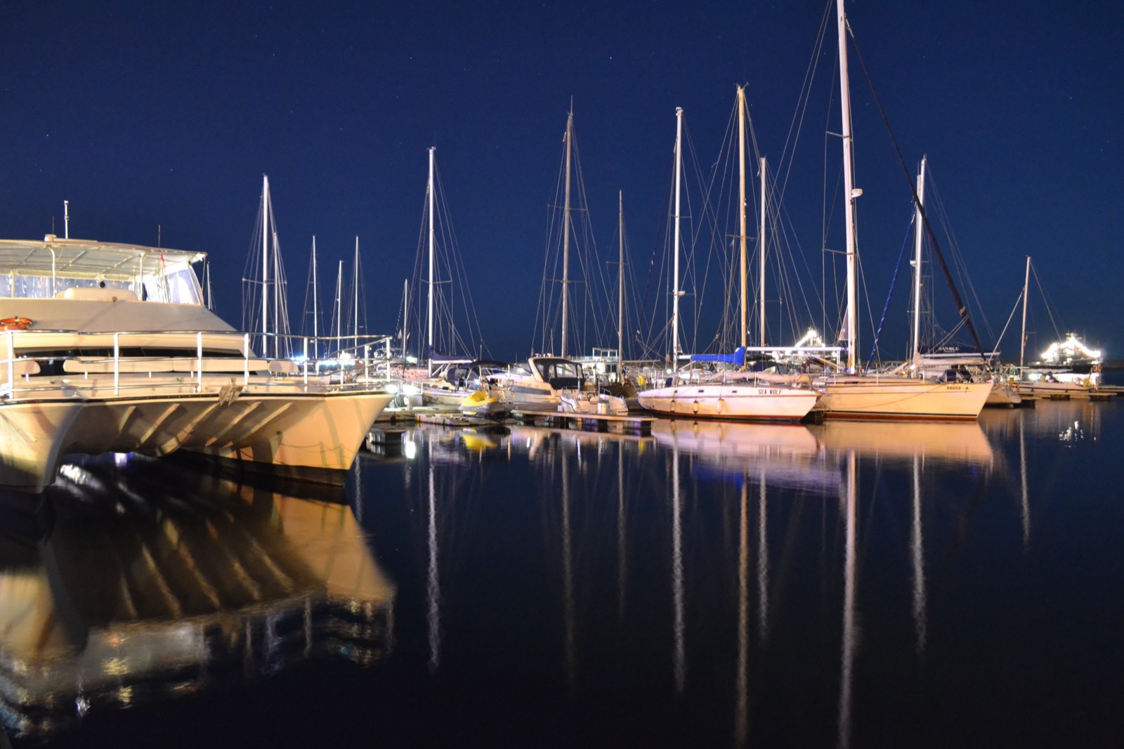 Iahturi luminate noaptea în portul turistic, reflectate în apa liniștită